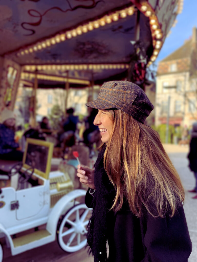 Photo de Anaëlle Adam en train de sourire proche d'un caroussel pour enfants.