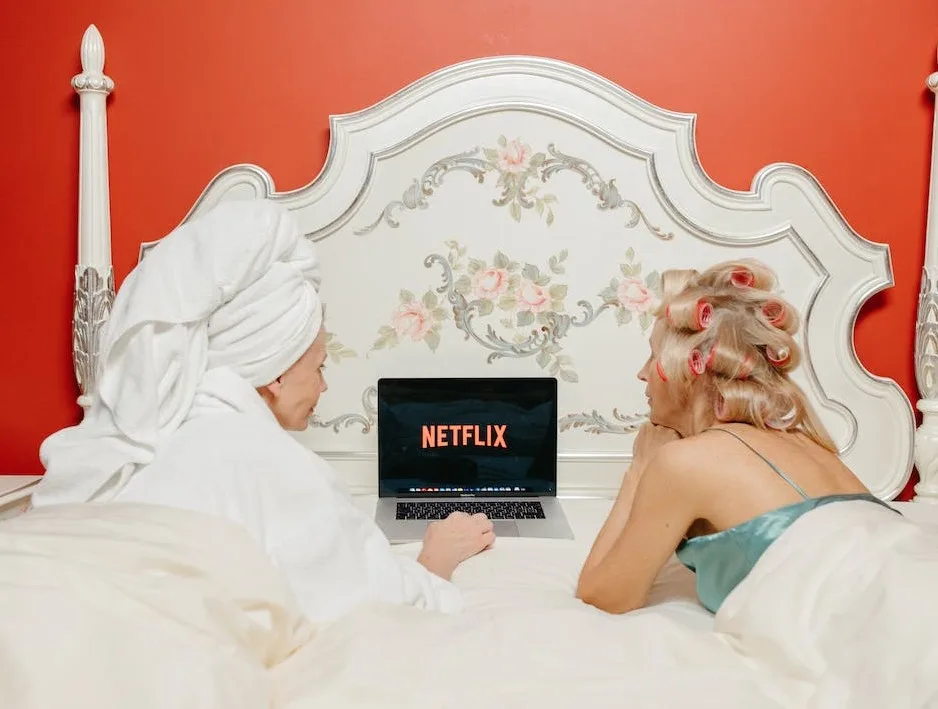 Deux femmes allongées sur un lit en peignoir qui regardent Netflix.